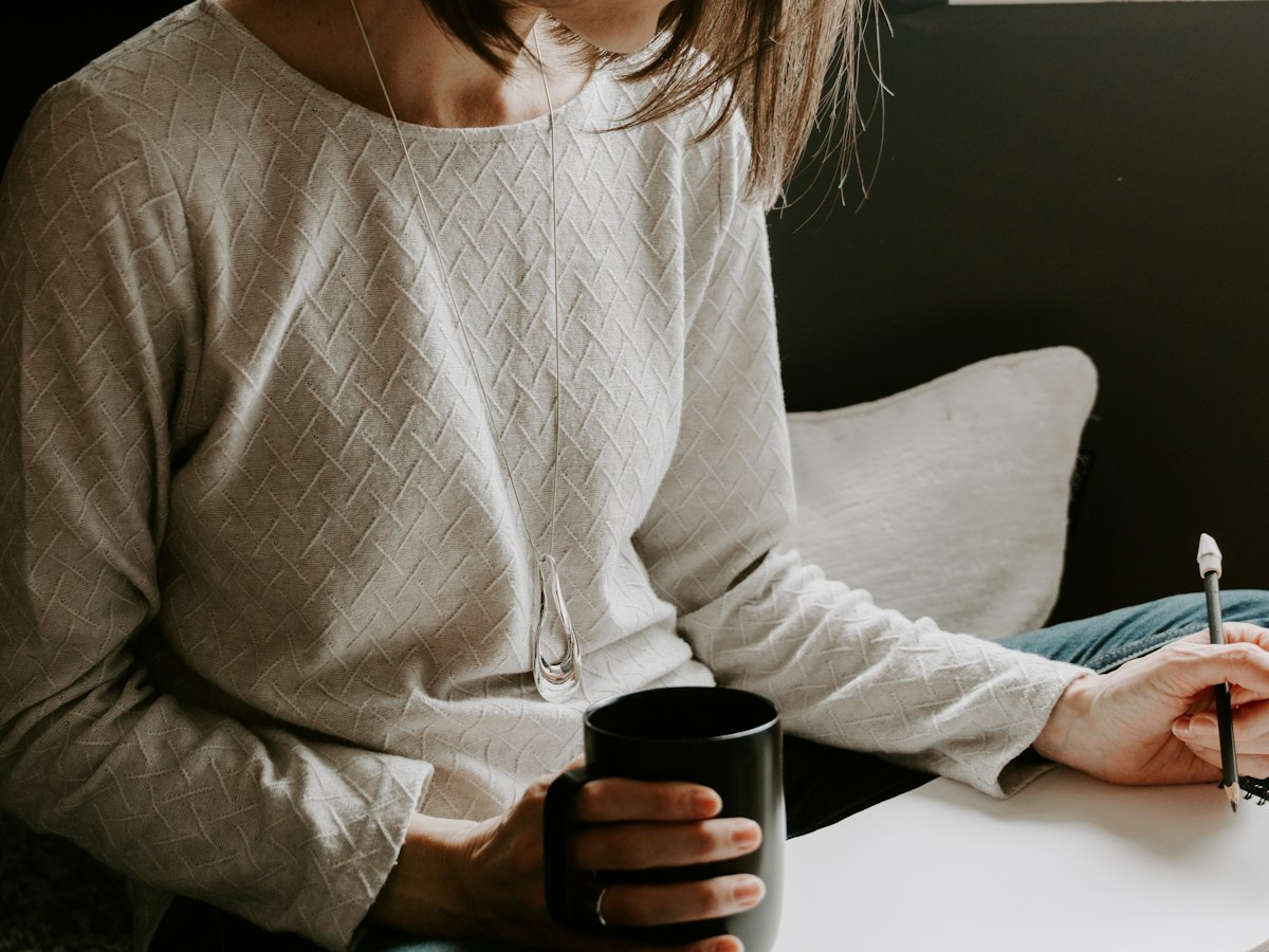 A woman writing in a notebook with a warm cup nearby
